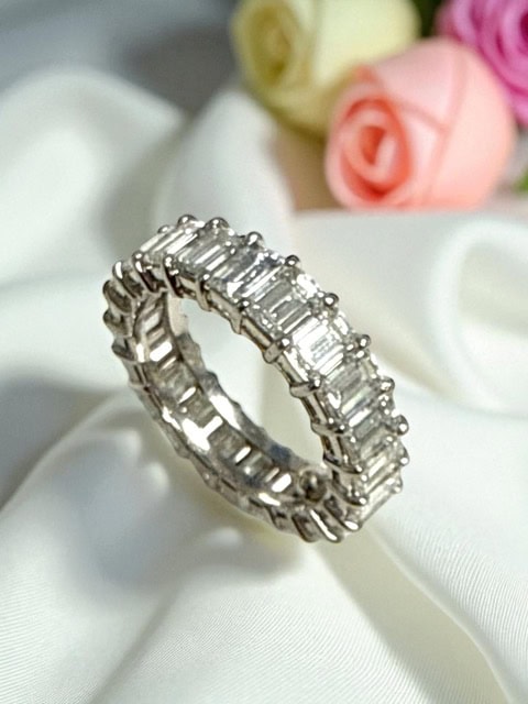 Elegant diamond eternity ring with baguette-cut stones on a satin fabric background.