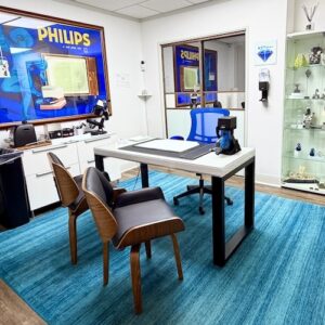 Modern jewelry office featuring display cases, a desk with a microscope, and a blue rug, ideal for buying and selling fine jewelry in a professional setting.