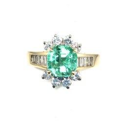 Elegant emerald and diamond ring with a central oval-shaped emerald surrounded by smaller diamonds, set in a yellow gold band with additional diamonds along the sides. Perfect for special occasions or as a luxurious gift. Rings
